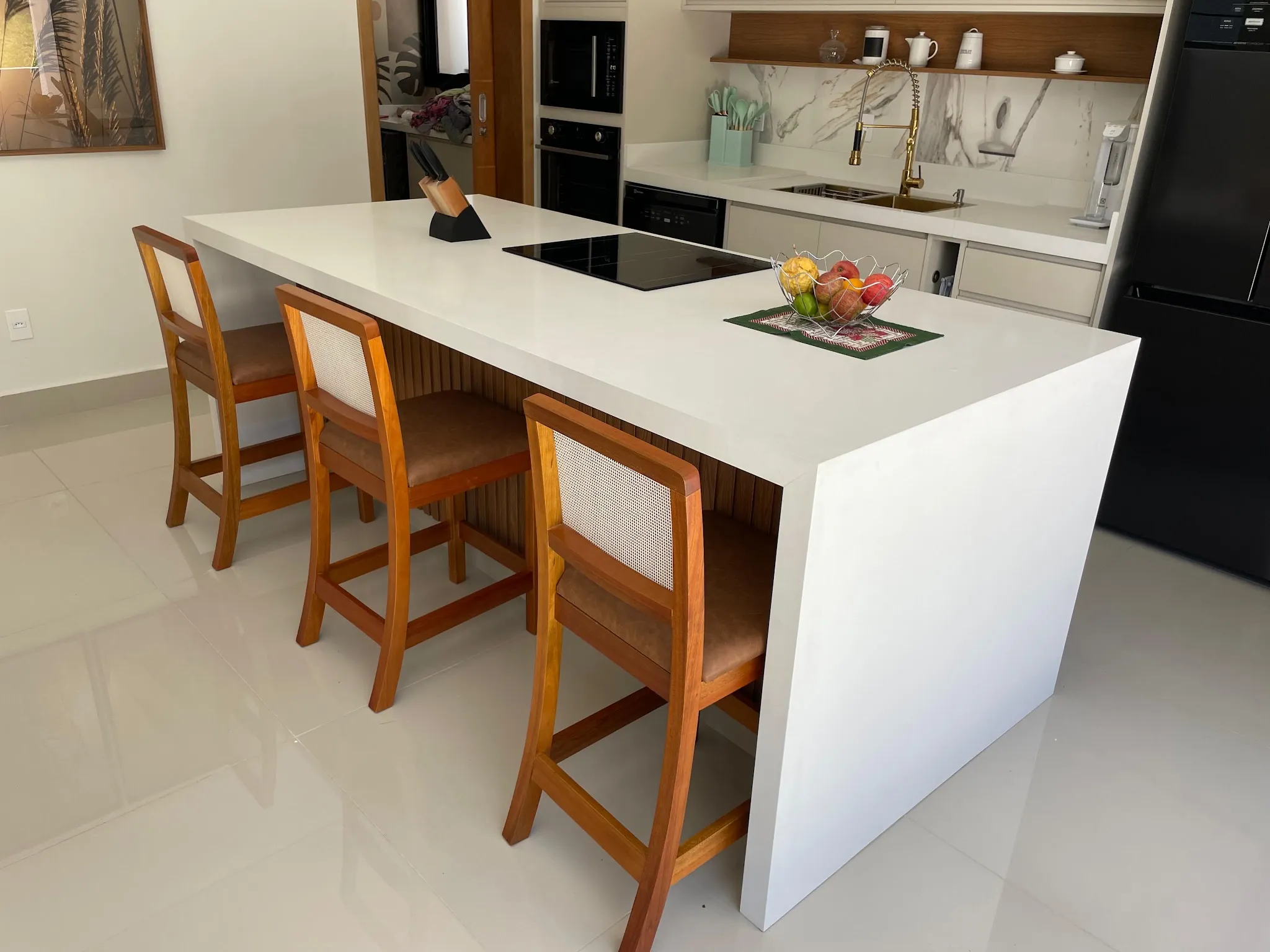Cozinha com ilha em porcelanato claro, banquetas de madeira e armários brancos